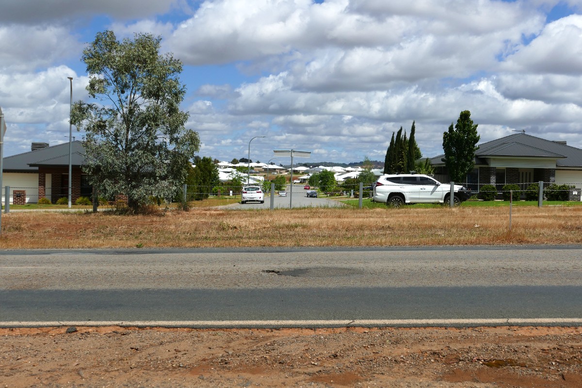 Road in the foreground, with suburban streets in the background and a white SUV travelling on one of the streets.