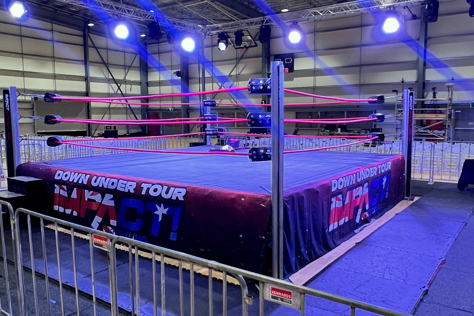 Wrestling ring in centre of indoor stadium, lit up purple.