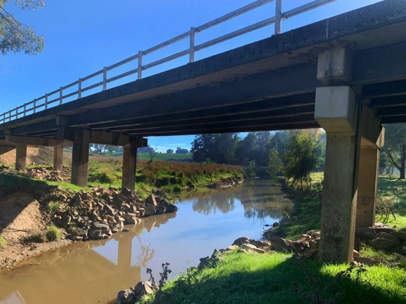 Steel and concrete bridge spanning a creek, with water in the creek bed.