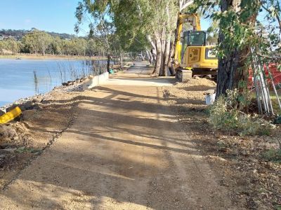 A yellow earth moving machine smoothing soil next to a newly installed concrete culvert, next to a lake.