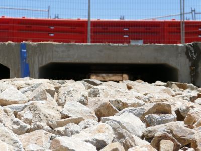 Large rocks in the foreground with a culvert under a roadway in the background.