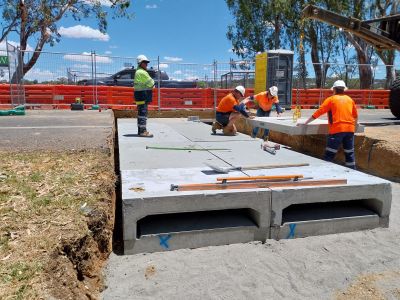 Four men in hi-vis shirts on a work site, working on the installation of large concrete culverts under a road.